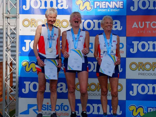 Jane Georghiou (left) with her medal and certificate on the podium with the GB65 ladies half marathon team at the 2023 European Masters (outdoor) Championships