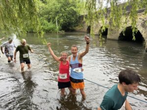 Leza Millington and Richard Denby standing in the River Wey crossing at the 2024 Elstead Marathon