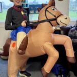 Sally Lawrence dressed as a cowboy on an inflatible pony at the 2024-25 Club Handicap race