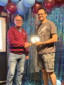 Justin Clarke presenting Ivan Chunnett with the men's award for the most PBs at the 2025 Farnham Runners AGM and awards evening