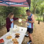 Nick Grist, running the 2025 Farnham Pilgrim marathon, stopping at a food and drink station provided by Farnham Runners, pictured with Gill Iffland