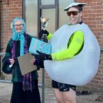 Harry May dressed as an egg receiving his trophy and prize from Jane Georghiou dressed as Mystic Meg at the 2025 Club Handicap race